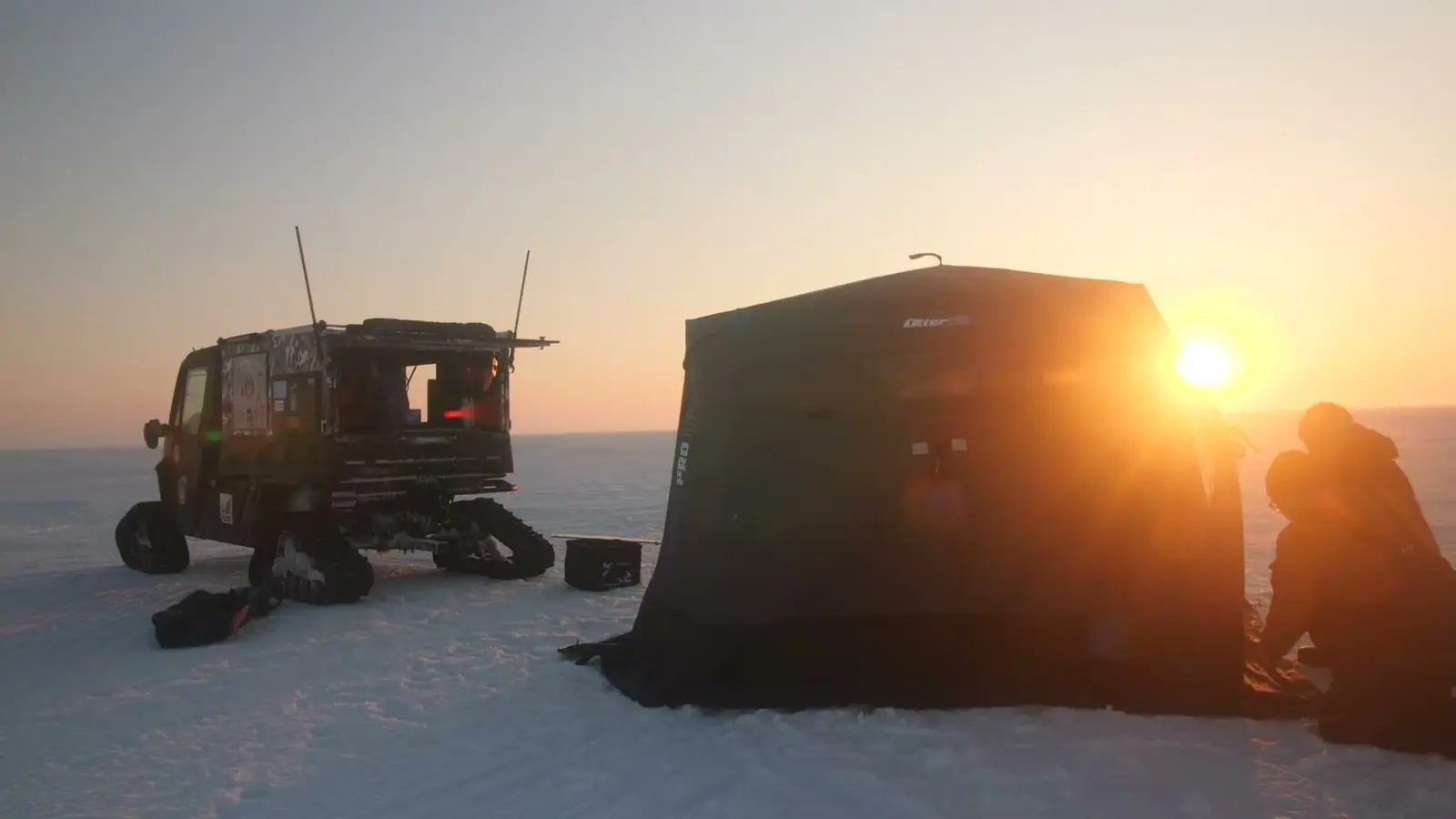 A shelter and the tracked UTV on open ice at sunset.