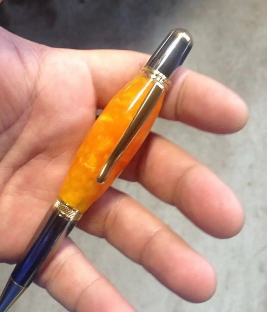 A pen with a marbled orange barrel, gold trim and a polished dark clip, held in an open palm.