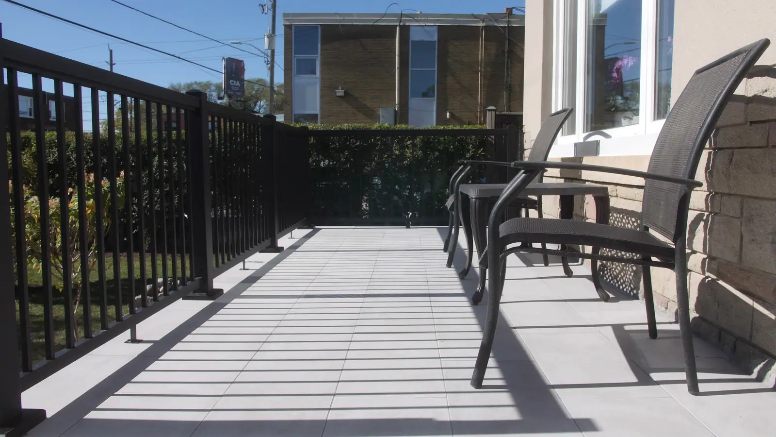 A finished porch landing of large pale slabs beside a black metal rail, with two chairs on the right.