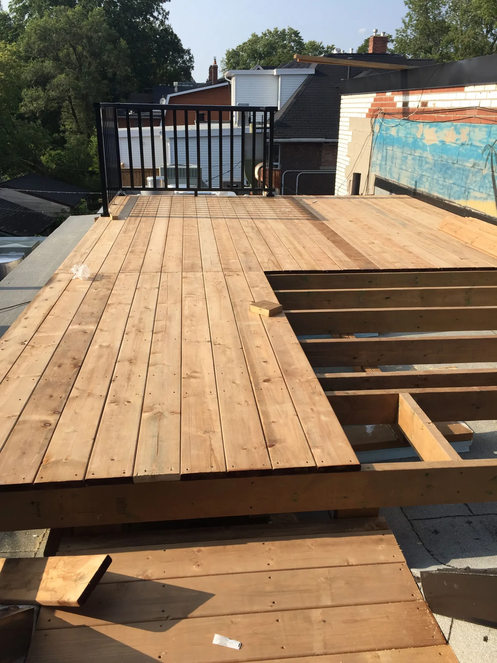 Deck boards being laid on a rooftop deck, with a framed cut-out still open.