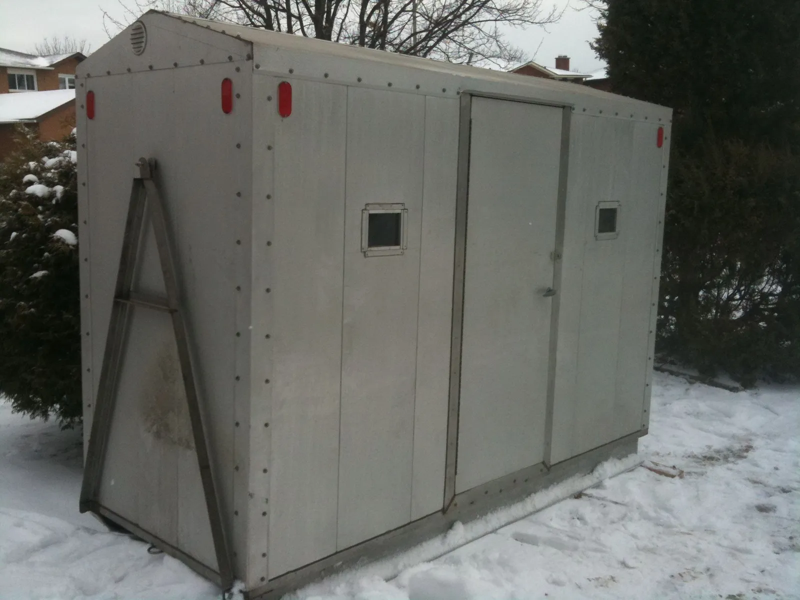 An aluminium-clad portable ice hut standing in snow.