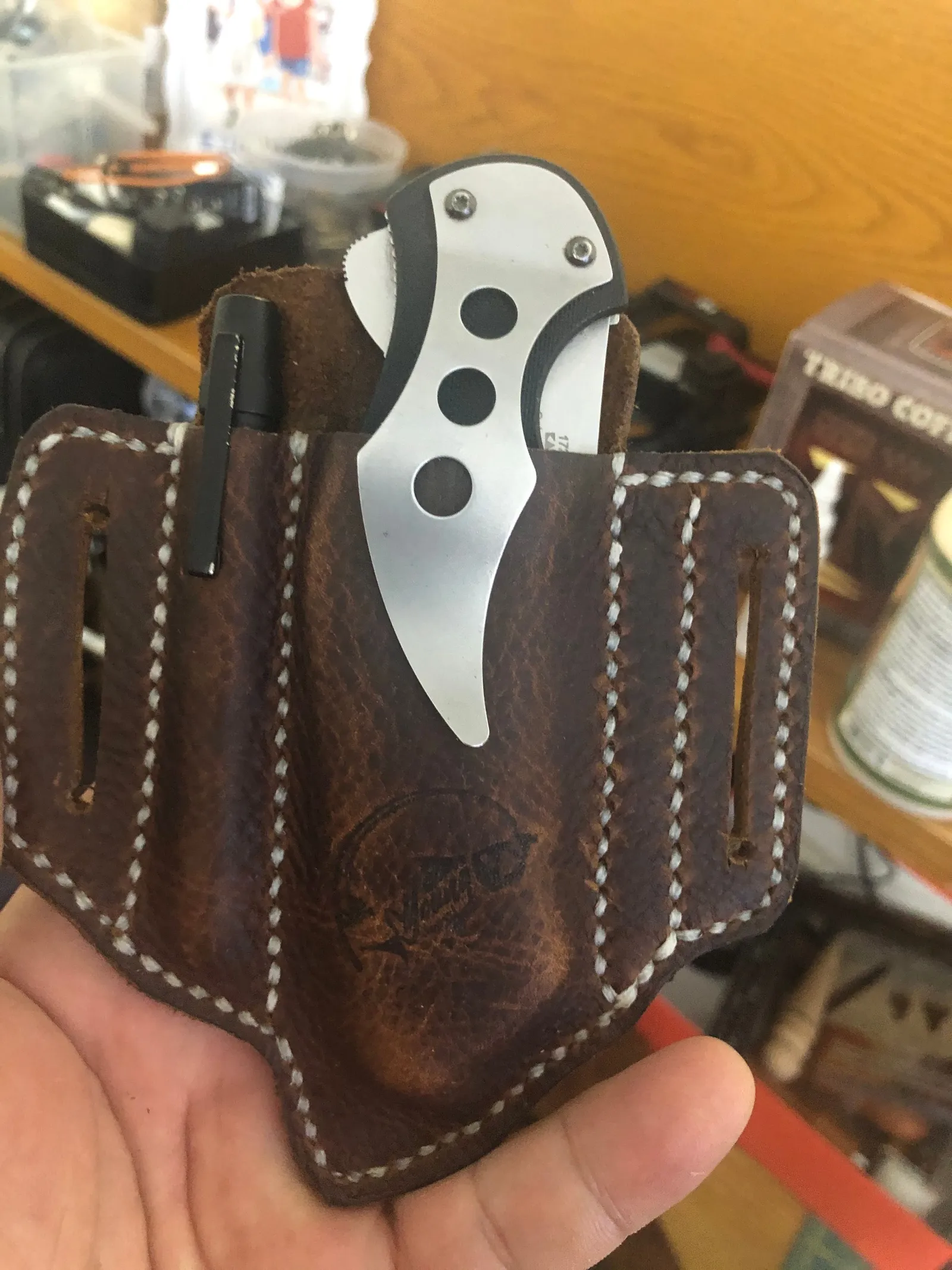 A leather knife sheath with a folding knife, held in a hand.