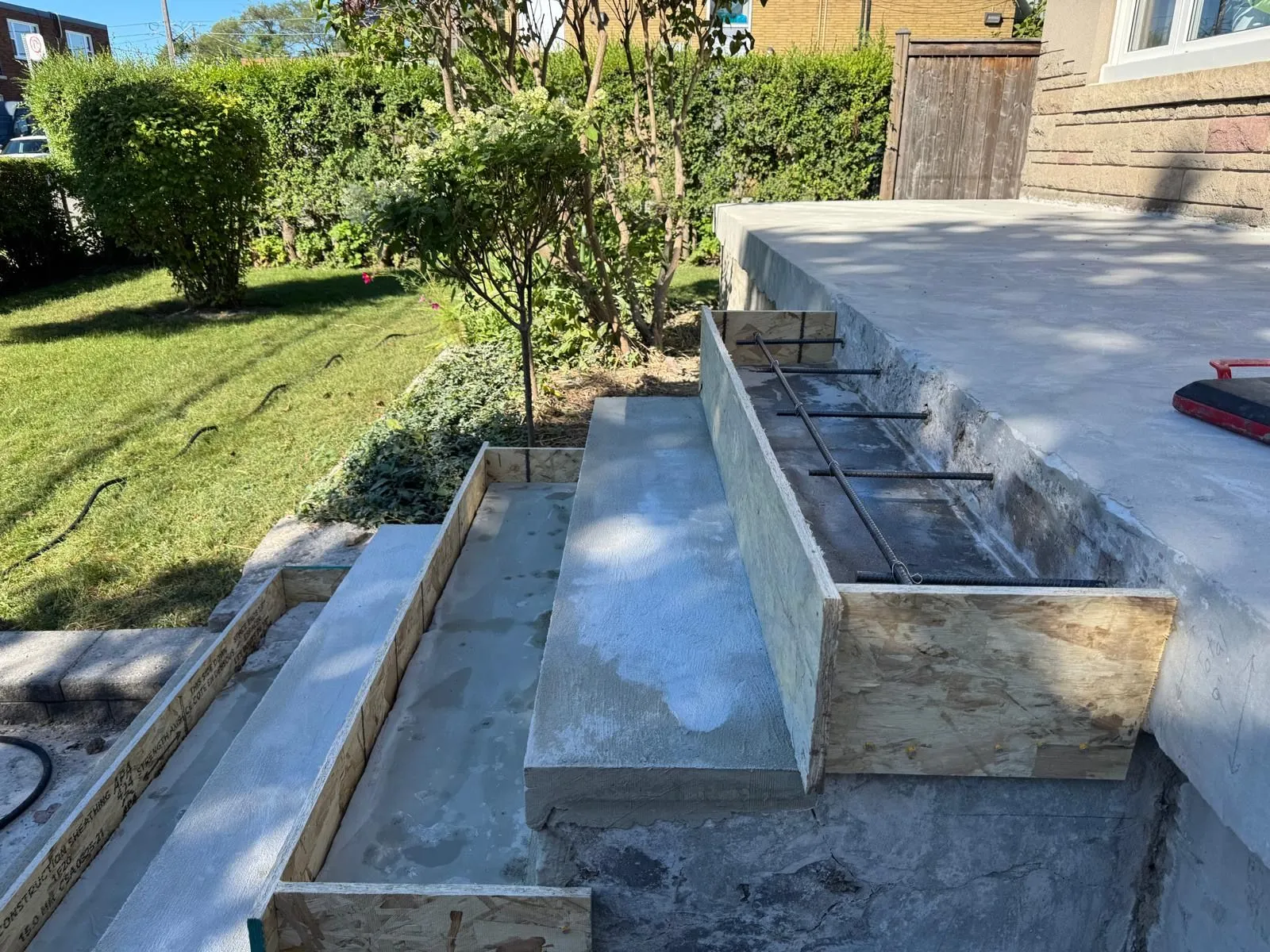 A new concrete landing and a timber form for a stepped wall with steel reinforcing bars, beside a lawn.