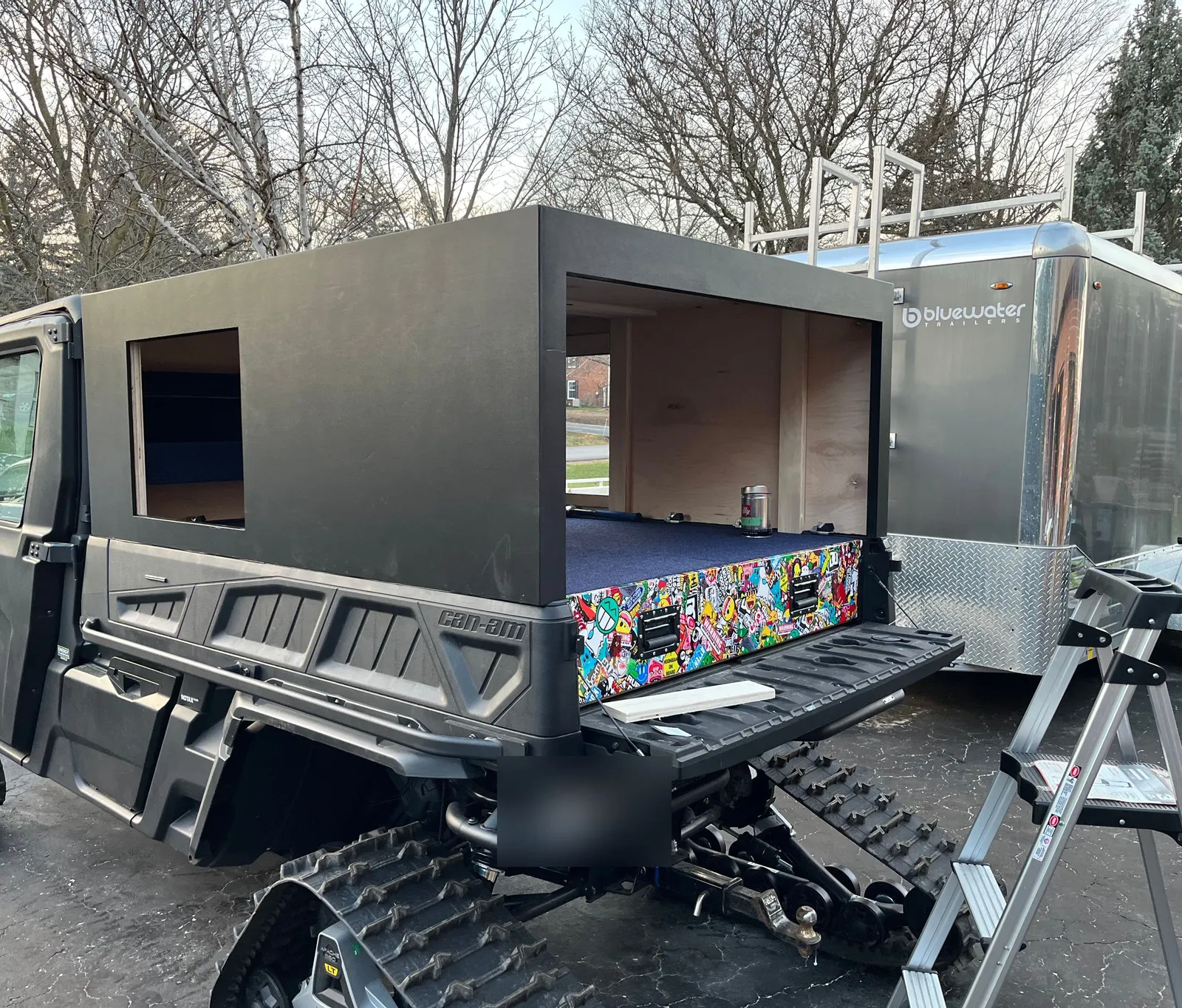 A black enclosed cabin on a tracked UTV, with a window and a plywood panel.